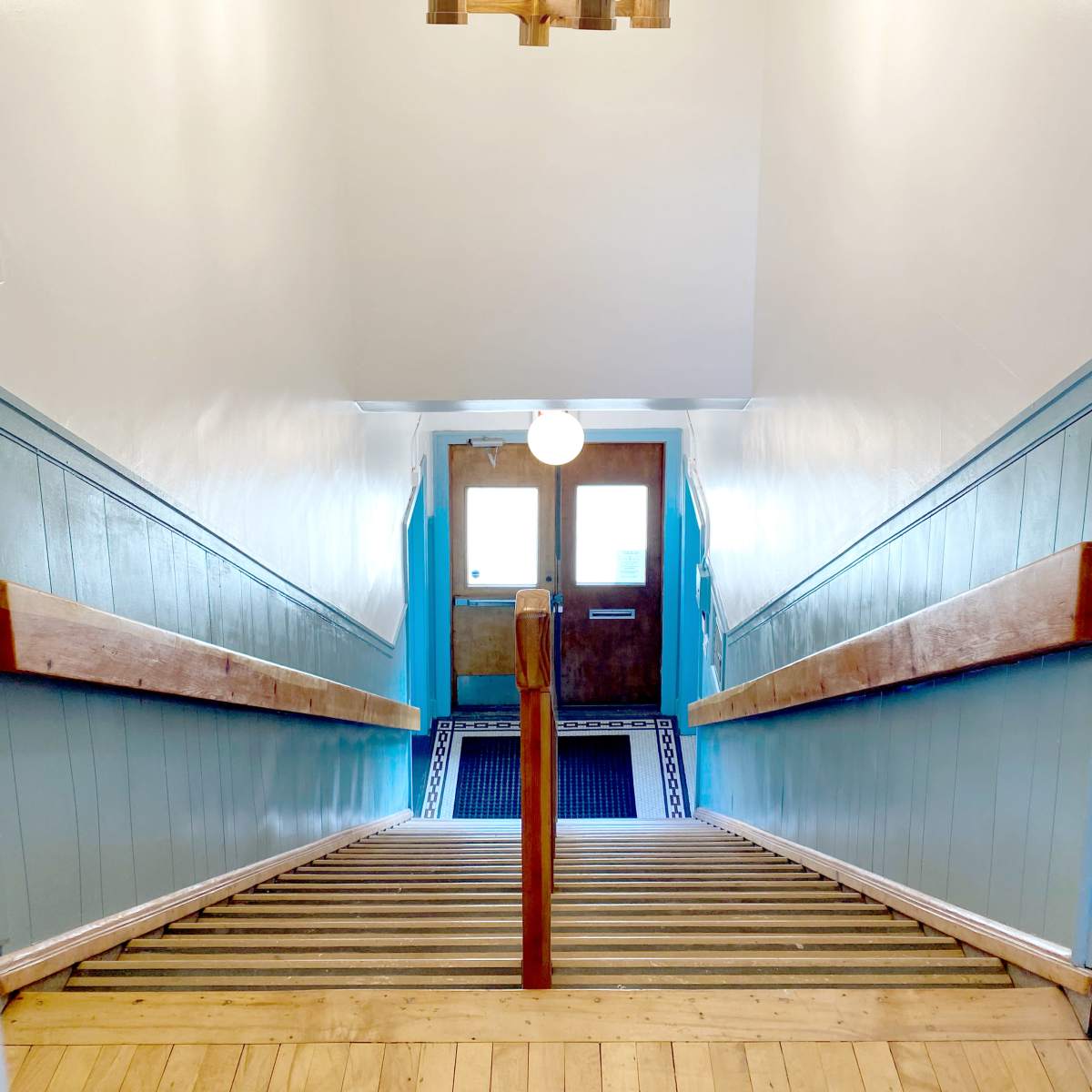 A well-lit stairwell with wooden steps leading downward to a door at the bottom.