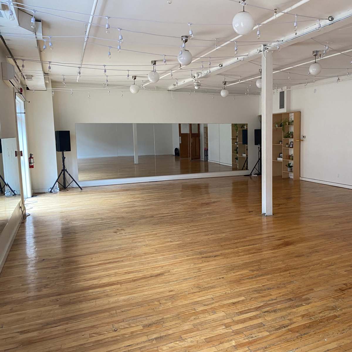 A spacious dance studio with polished wooden floors, large mirrors, and bright overhead lighting.