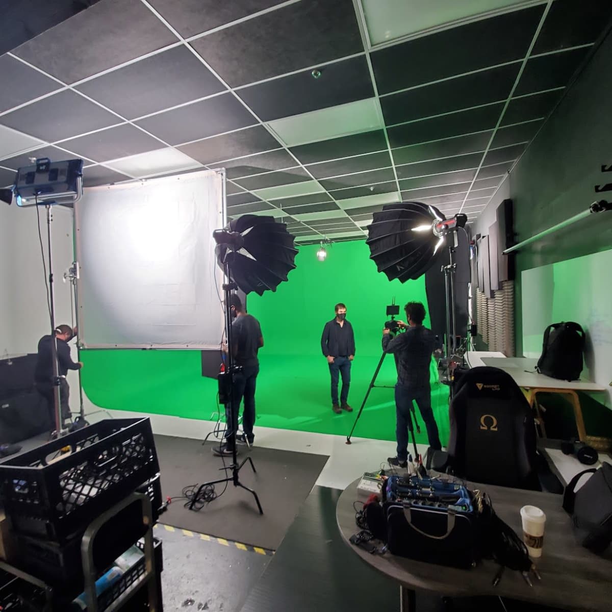 A film crew sets up equipment in a green screen studio for a video shoot.