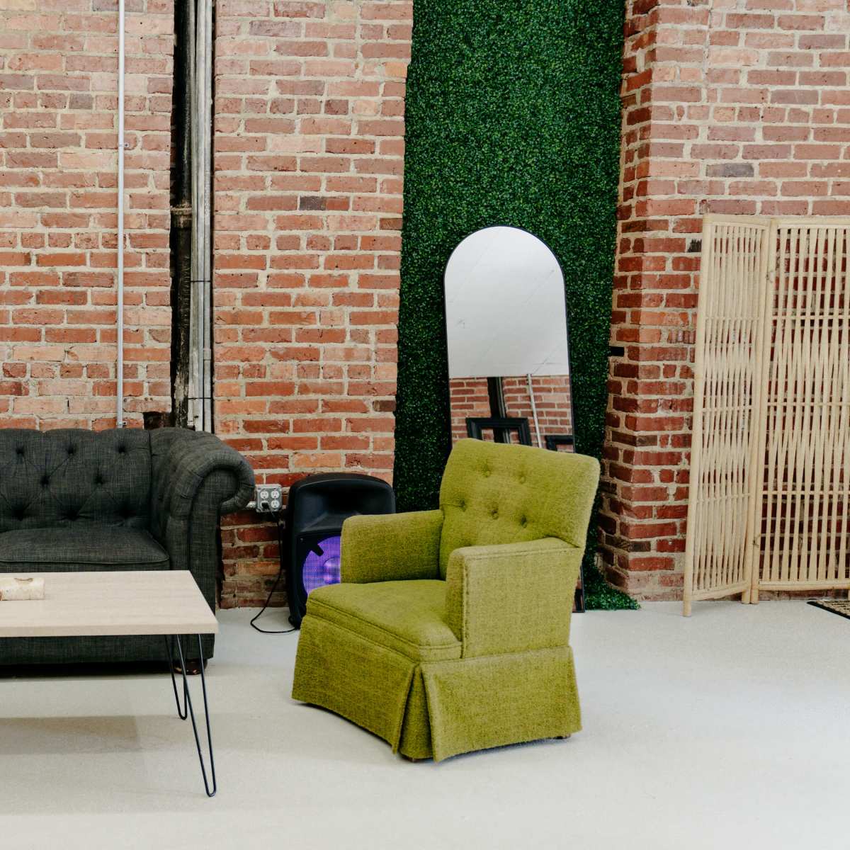 A modern interior with a black tufted sofa, a green upholstered armchair, a wooden coffee table, and exposed brick walls.