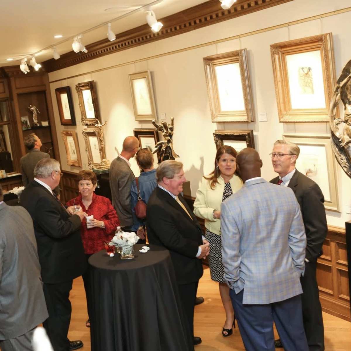 A group of people mingles at a gallery opening, surrounded by artwork and elegant decor.