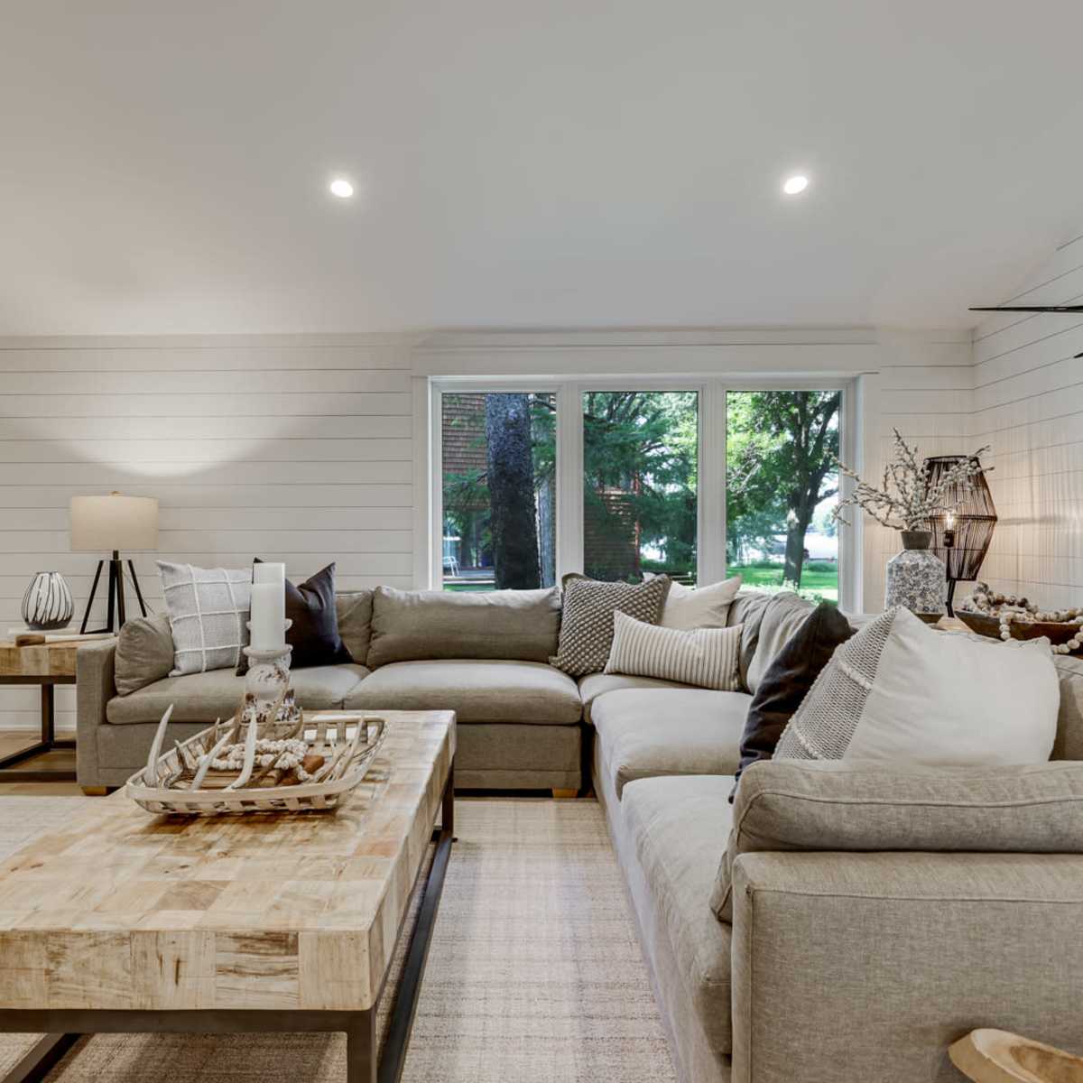 The living room features a sectional sofa, a wooden coffee table, a decorative sailboat, and a mounted deer head against light-colored walls and large windows.