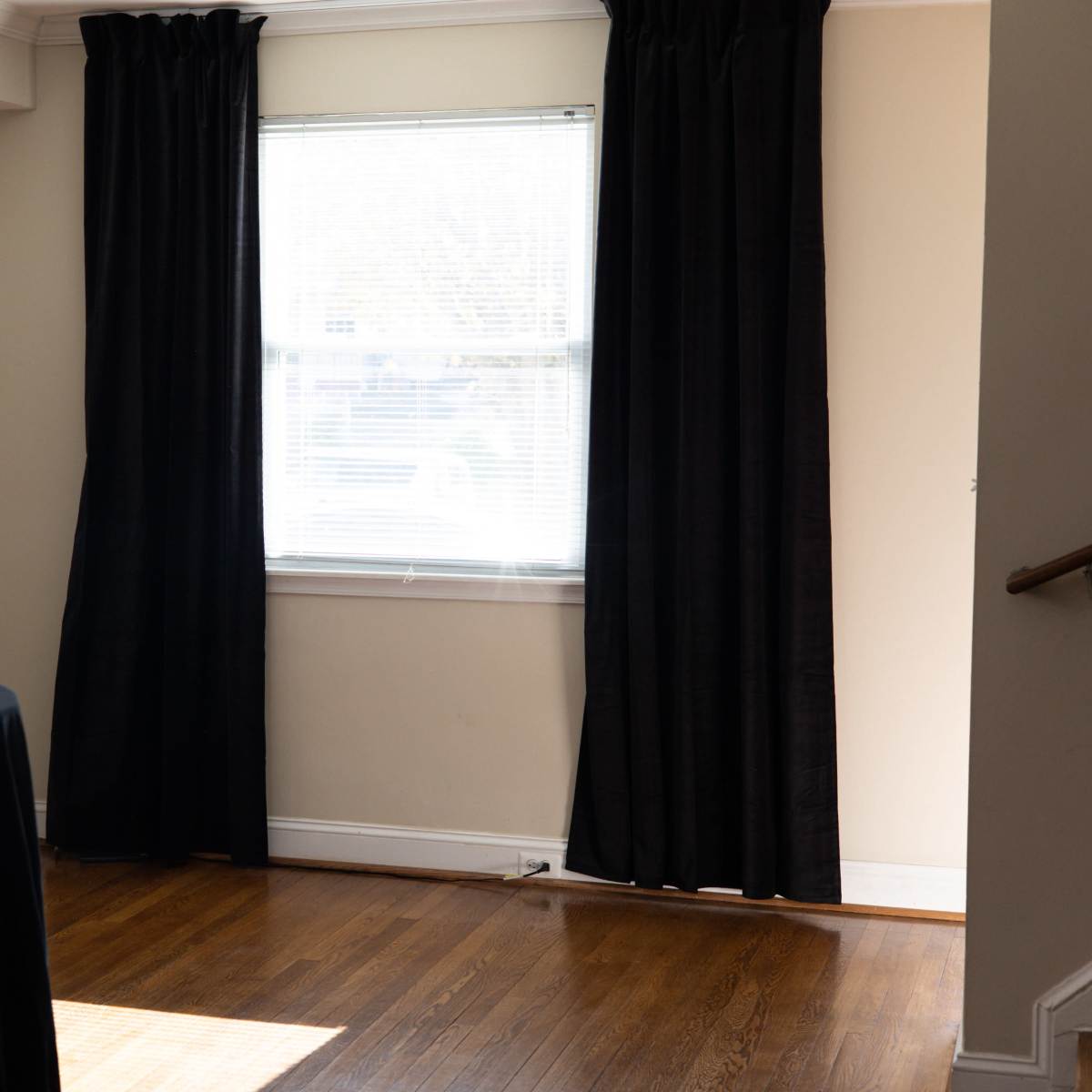 A room with hardwood flooring, a black table in the center, and curtain-covered windows, alongside a television on the wall displaying colorful graphics.