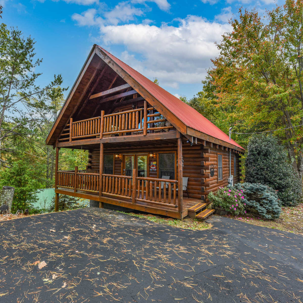 A wooden cabin with a sloped roof, adorned with balconies, is surrounded by trees and autumn foliage.