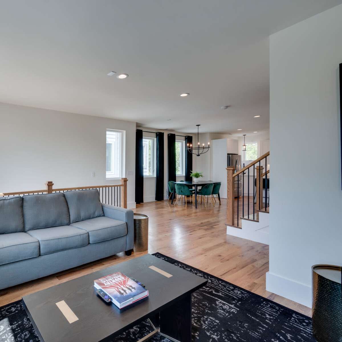 A spacious living room features a gray sofa, hardwood floors, and large windows that allow natural light to illuminate the space.