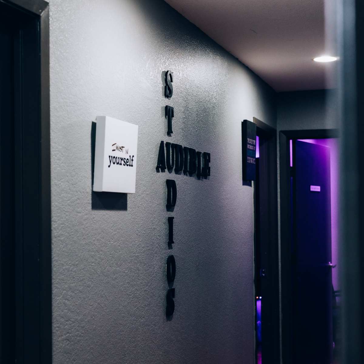 A dimly lit hallway features doors on either side, with a sign that reads "AUDITION STUDIO" prominently displayed on the wall.