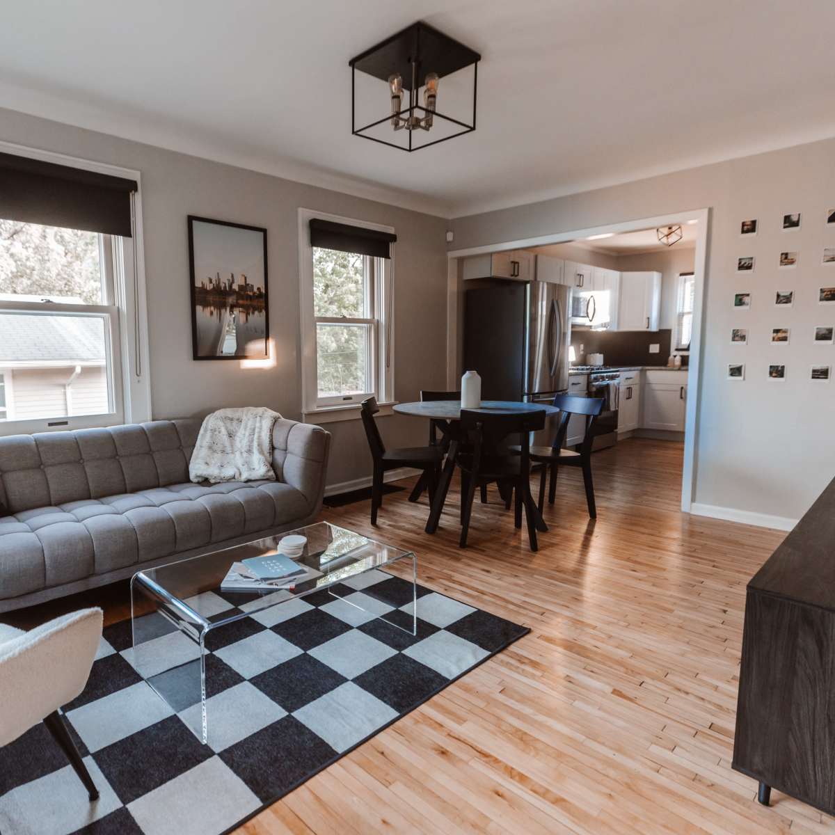 The living room features a gray couch, a black and white checkered rug, and a glass coffee table, with a dining area visible in the background.