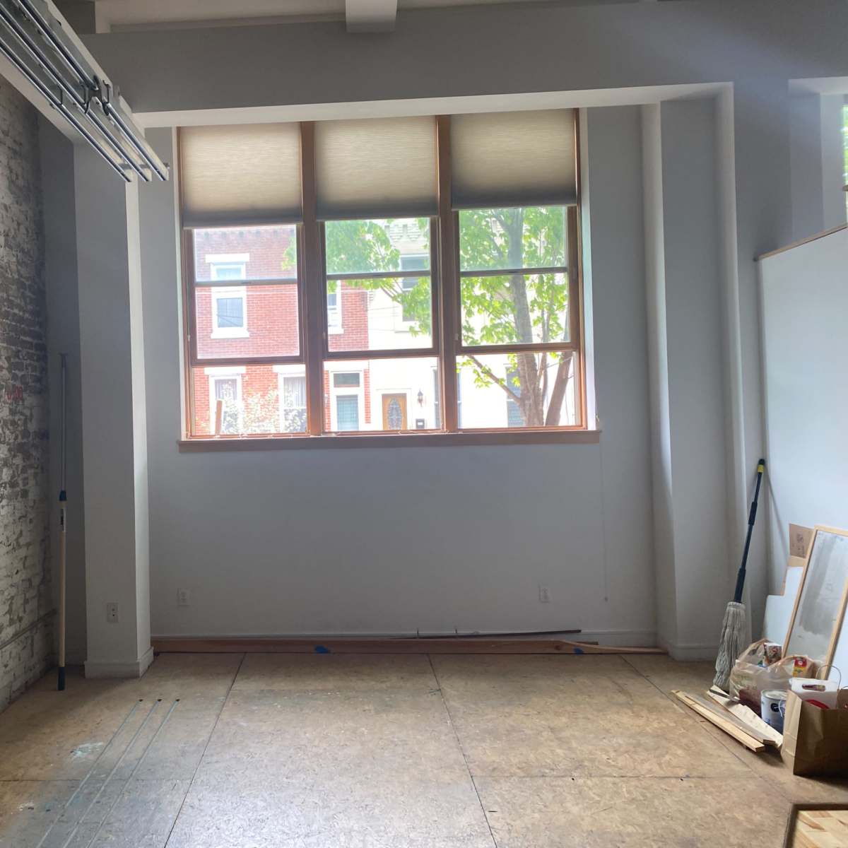 An empty room with a brick wall on one side and large windows overlooking a street with houses outside.