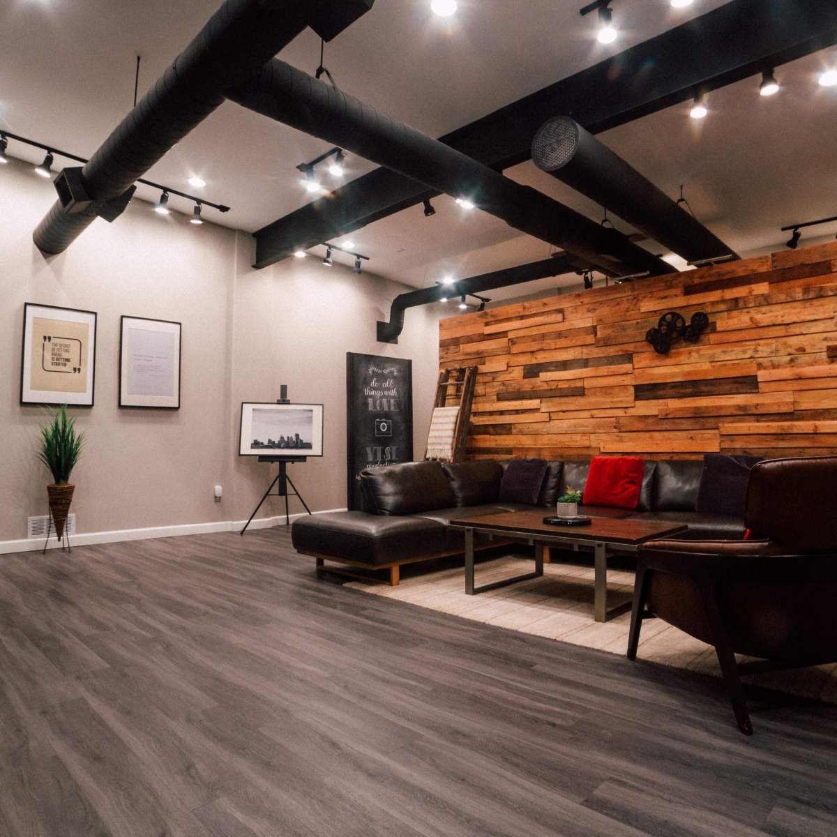 A modern living room features a brown leather sectional sofa, wooden accent wall, and various framed artworks.