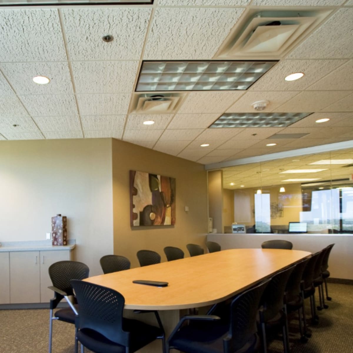 A conference room features a large table surrounded by chairs, with a television mounted on the wall and windows providing a view of the outside.