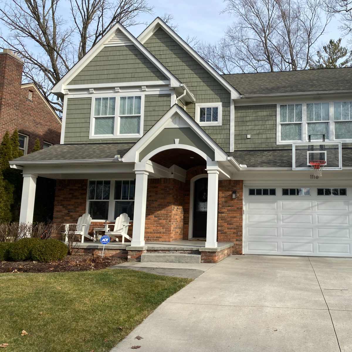 A two-story house with gray siding and brick accents features a front porch and a basketball hoop mounted on the garage.