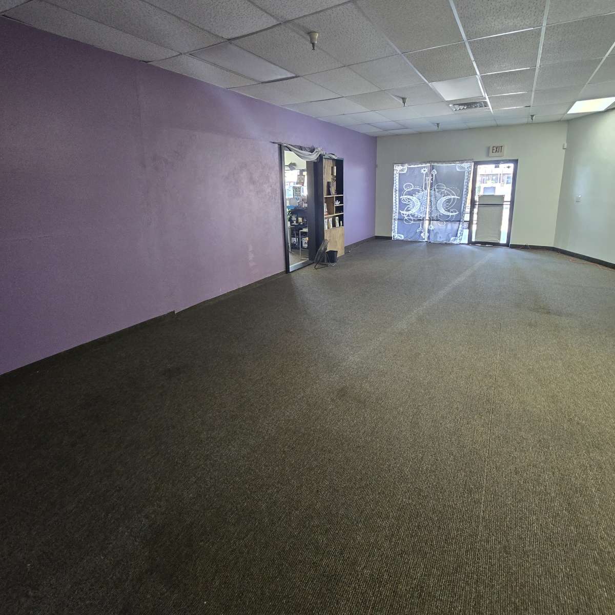An empty room with purple walls and a carpeted floor, featuring a door on one side leading to an adjacent space.