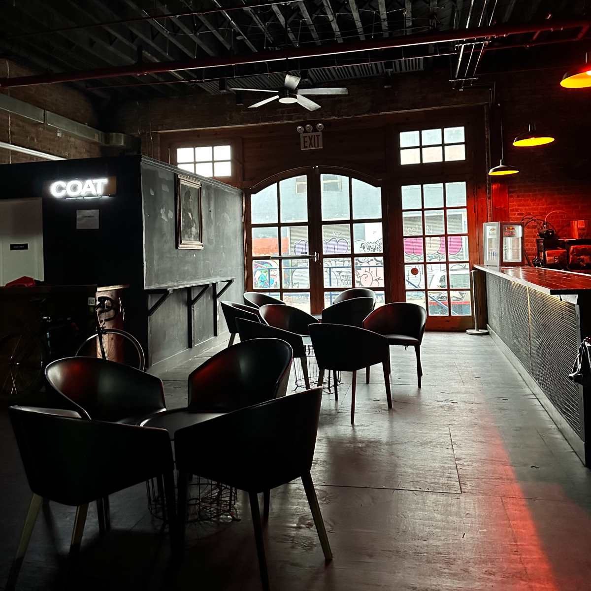 A dimly lit bar area with several black chairs and a large window revealing an outdoor view.