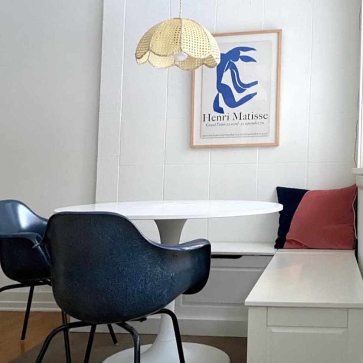 A dining area with a round white table, black chairs, a woven pendant lamp, and a framed artwork by Henri Matisse on the wall.