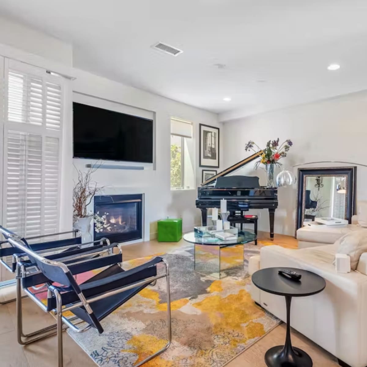 The living room features a piano, modern furniture, and a fireplace with artwork displayed on the walls.