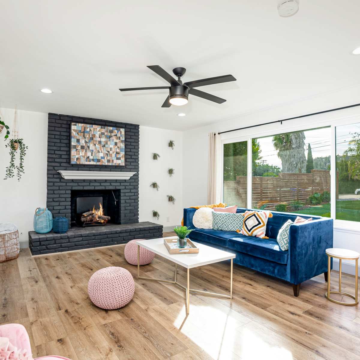 The living room features a blue velvet sofa, a modern coffee table, a fireplace surrounded by black brick, and large windows letting in natural light.