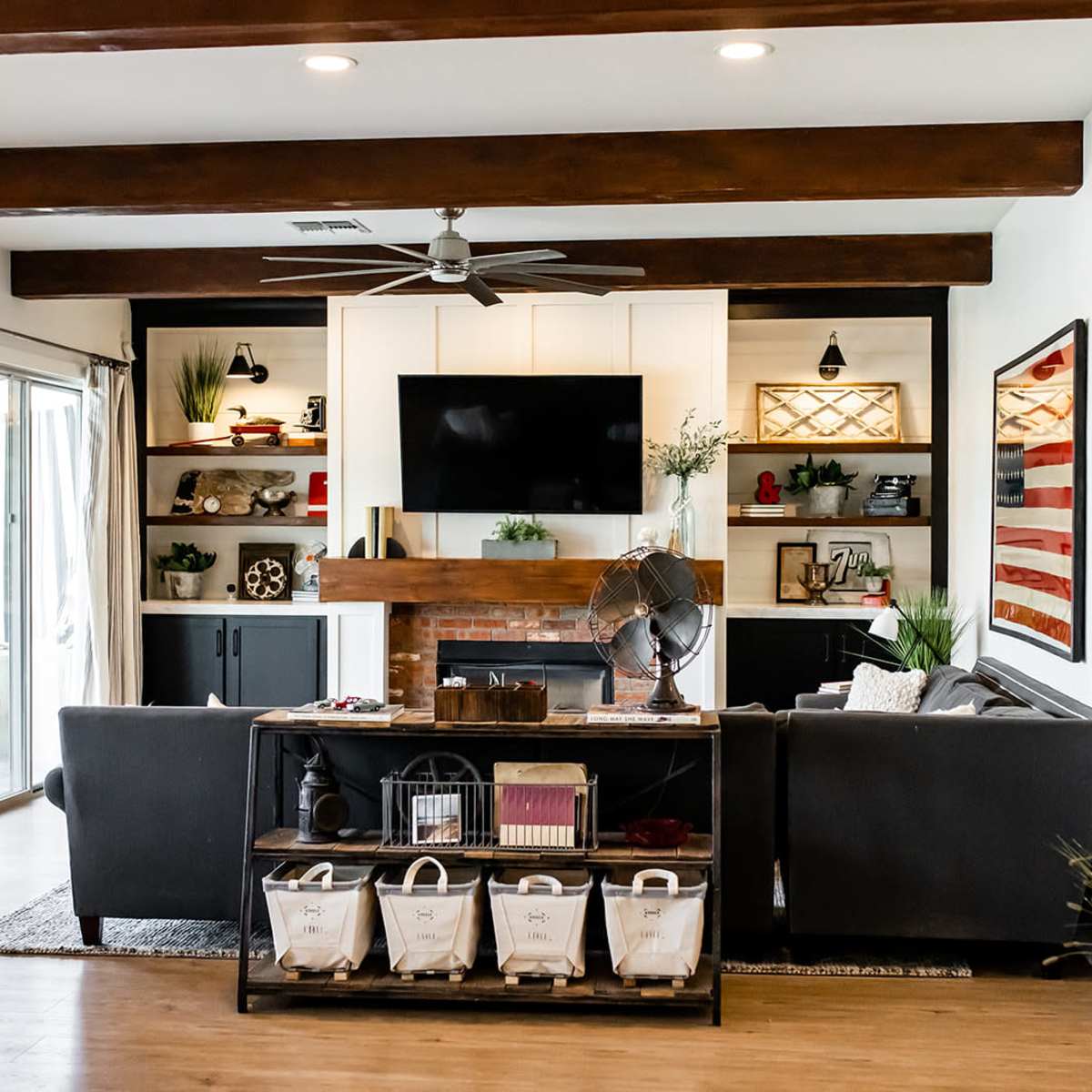 The living room features a black sofa, a wooden coffee table with storage bins, and a wall-mounted TV above a fireplace, surrounded by built-in shelves with decorative items.