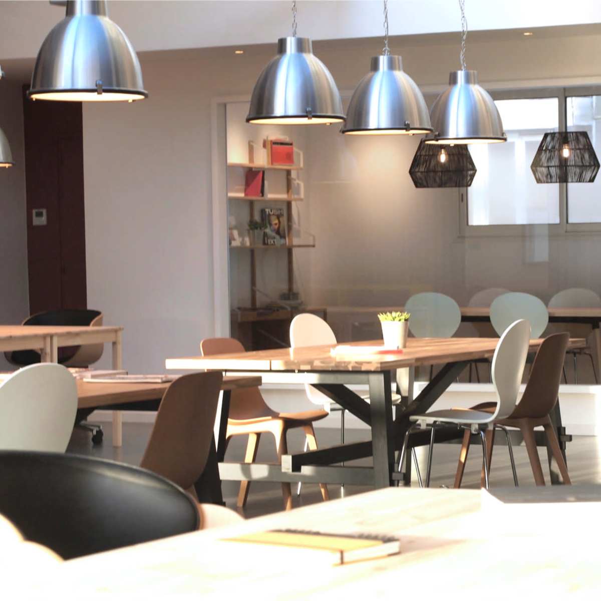 A modern office space with wooden tables, various chairs, and pendant lighting.