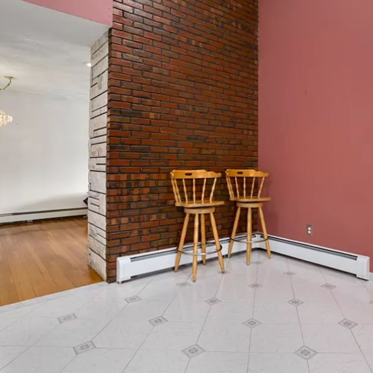A room with a brick wall, two wooden stools, and an entrance leading to another area with hardwood flooring.