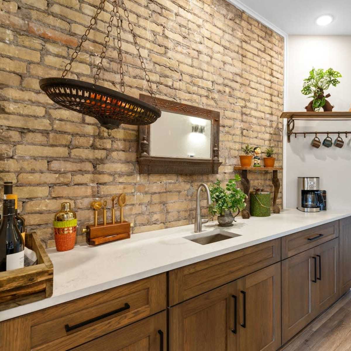 A hallway with a brick accent wall, a wooden countertop featuring a sink, and various plants and kitchen items arranged on shelves above.