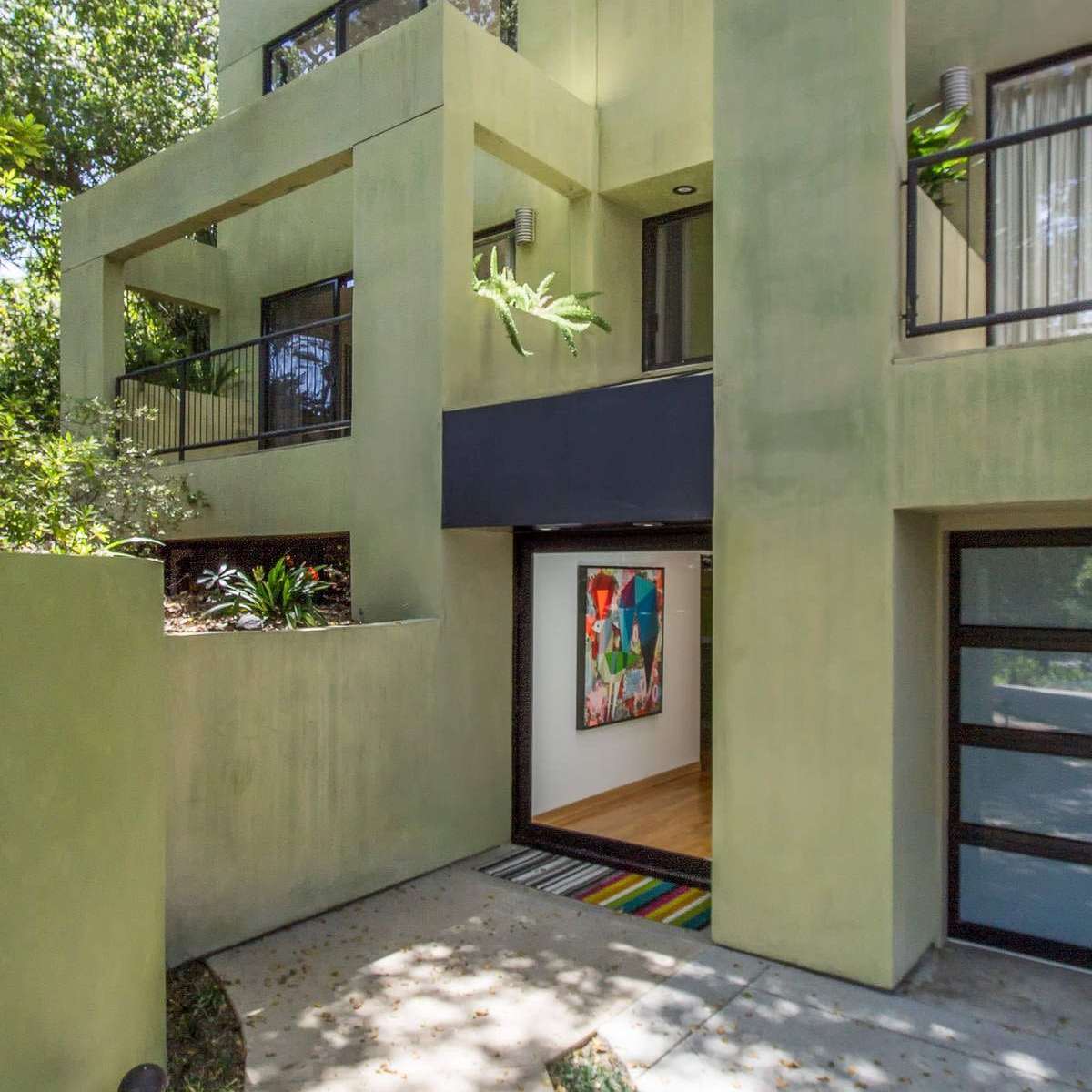 A modern, multi-level house with a green exterior and large windows surrounded by trees.