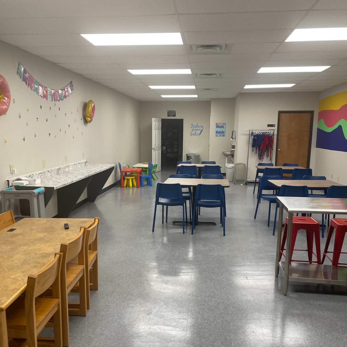 A spacious classroom with several tables and chairs arranged neatly, along with colorful wall decorations and a water cooler.