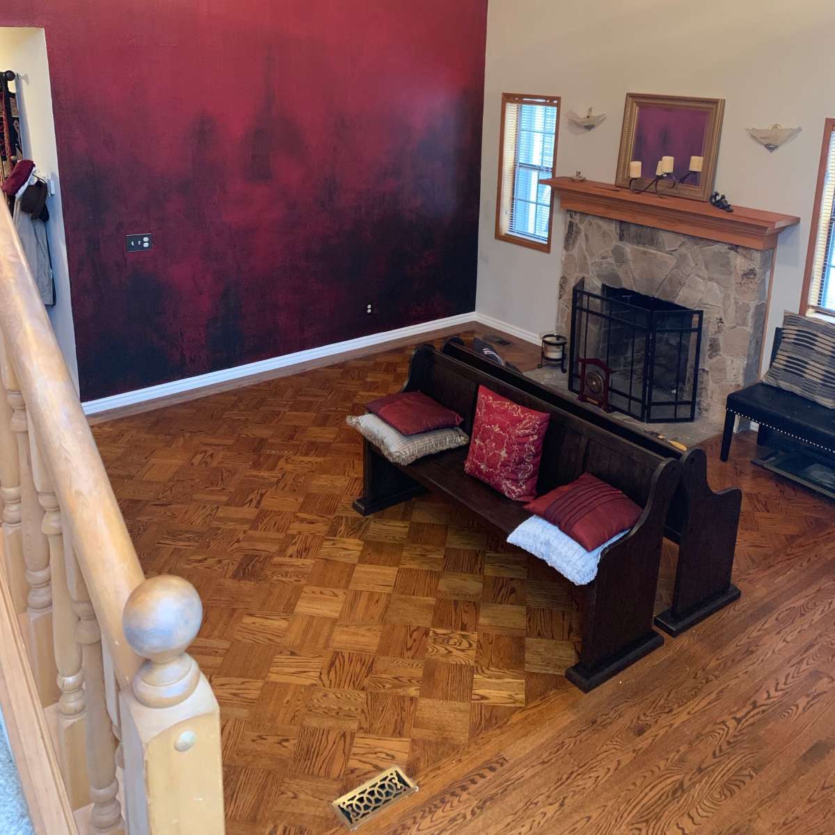 A spacious living room with a red accent wall, a wooden bench with cushions, and a stone fireplace.