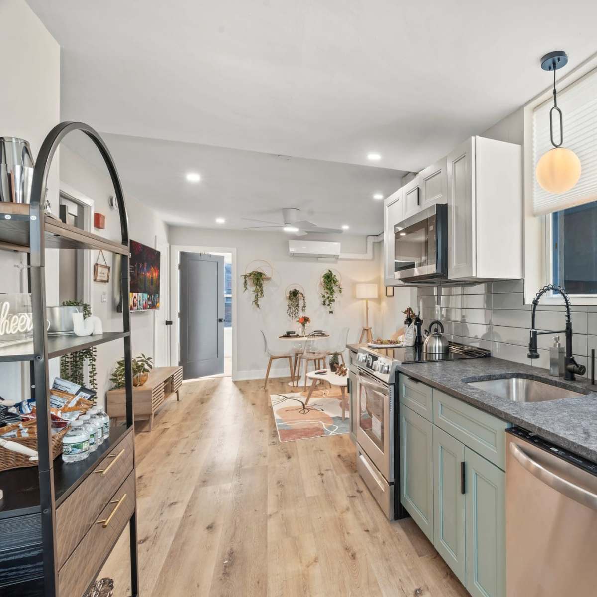 A modern kitchen with light cabinetry, a dark countertop, and stainless steel appliances, leading to an adjacent dining area.