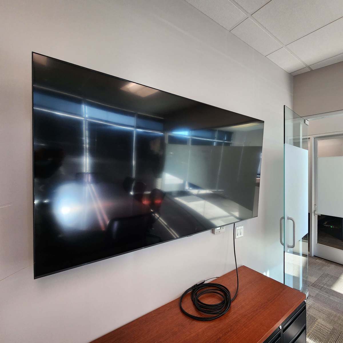 A large flat-screen television mounted on a wall beside a glass partition in a modern office space.