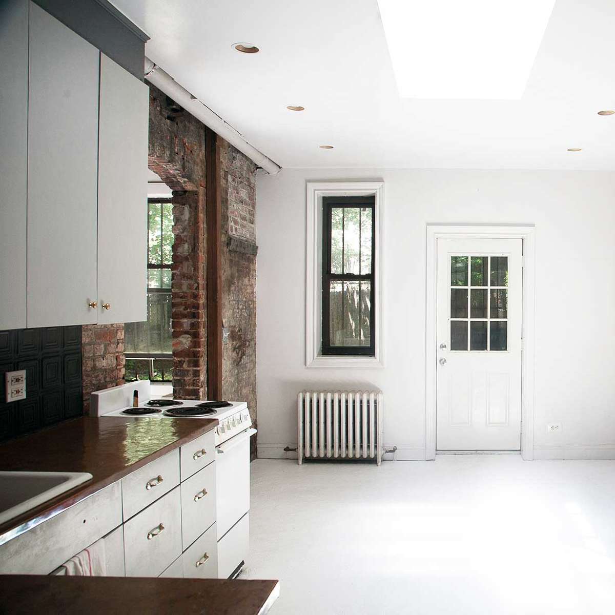 A minimalist kitchen and living area with exposed brick walls, a white ceiling, and a door leading outside.