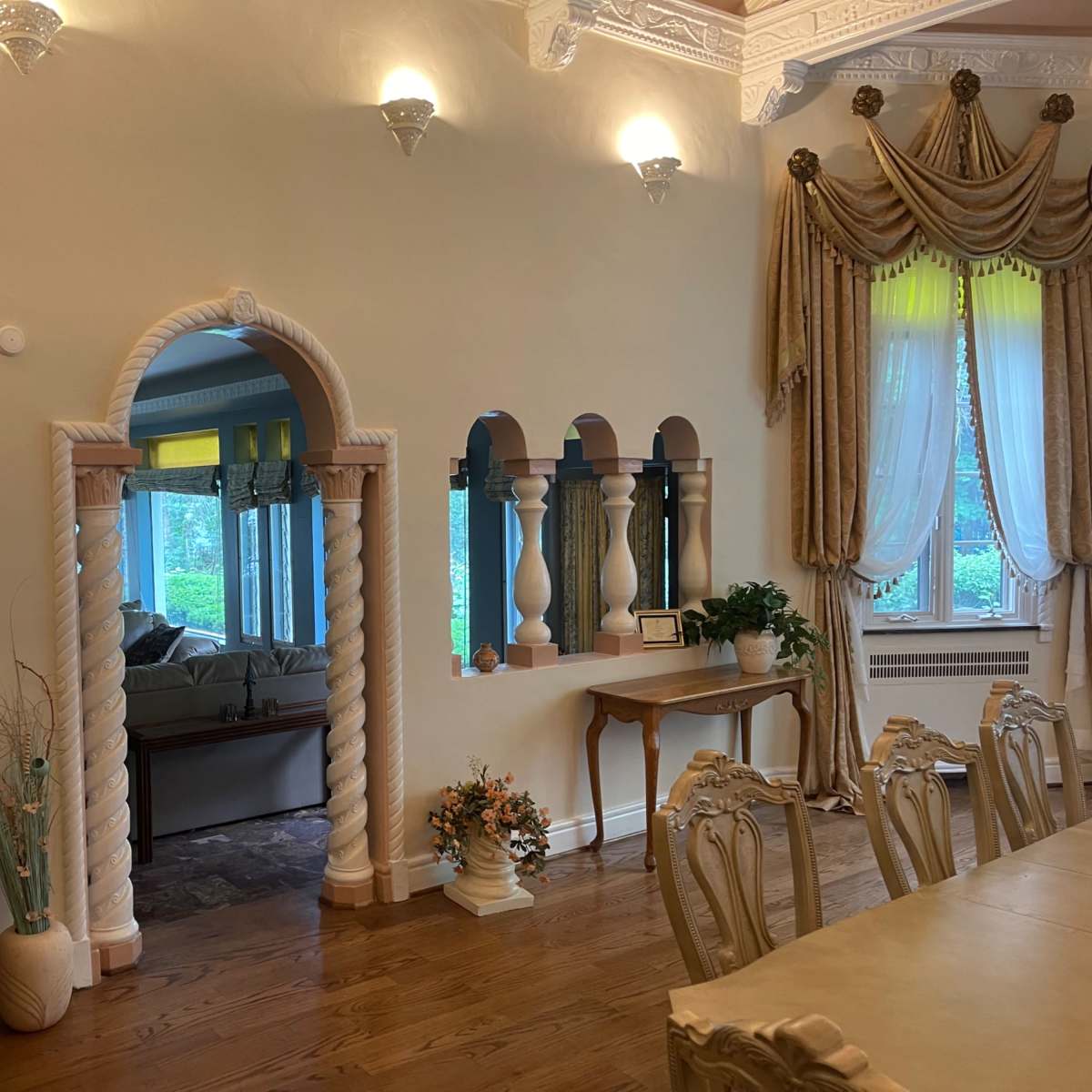A dining area with elegantly designed arches and columns, leading to a well-lit living space beyond.