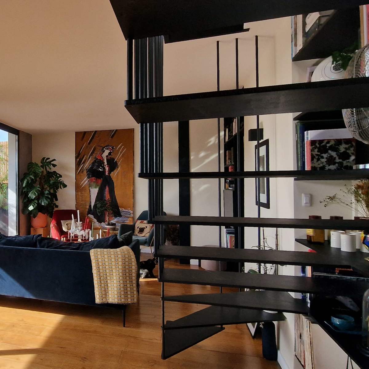 A modern, open-plan living space featuring a spiral staircase, large windows with outdoor views, and a mix of seating areas.