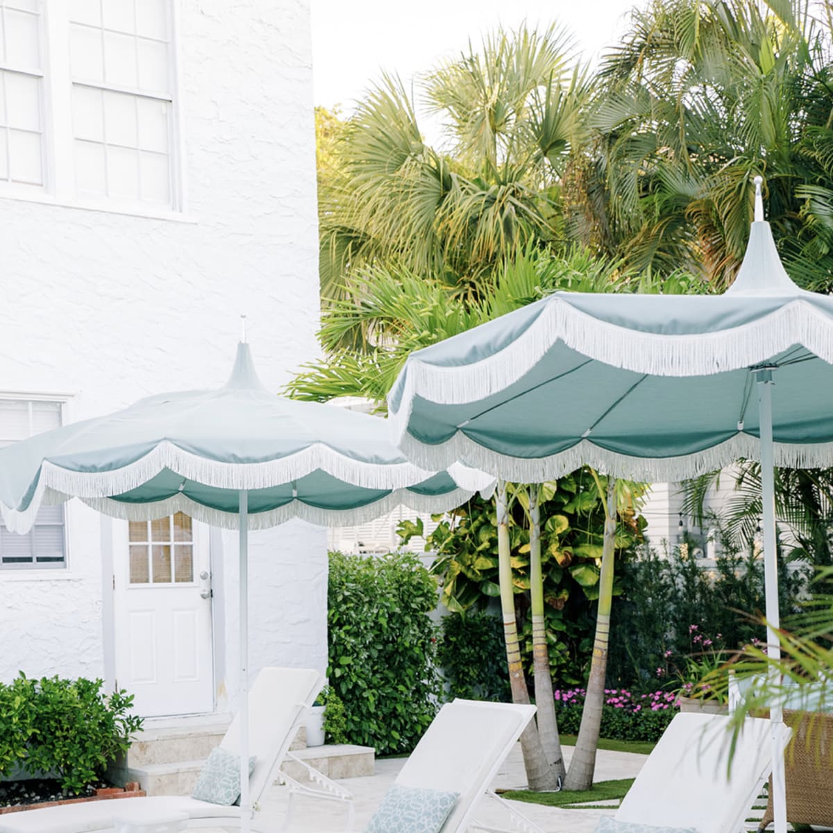 A serene pool area with white lounge chairs and teal-striped umbrellas surrounded by lush greenery.