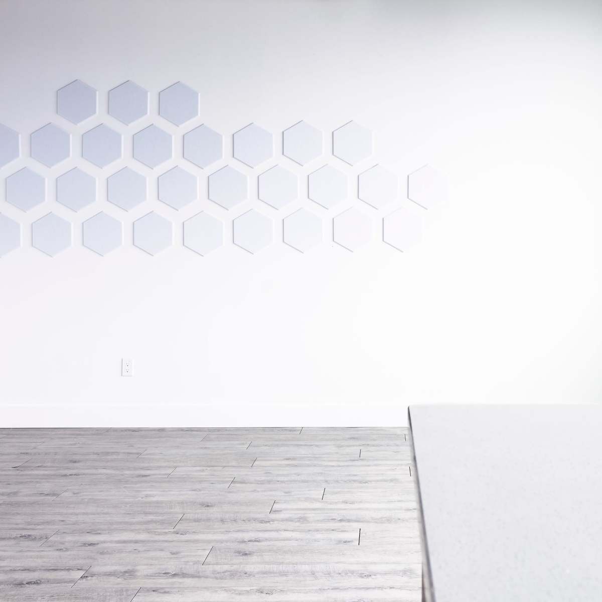 A minimalist room featuring light-colored walls, a geometric hexagon pattern on one wall, and a large window with natural light illuminating a light wood floor.