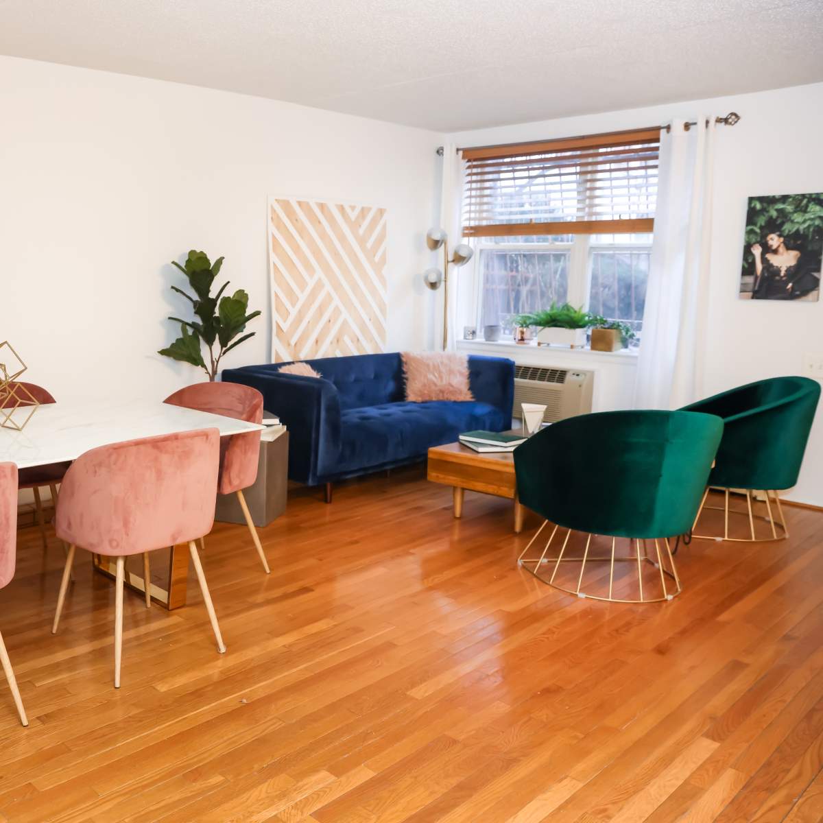 A dining area with a marble table and pink upholstered chairs, adjacent to a living space featuring a blue sofa and green accent chairs.