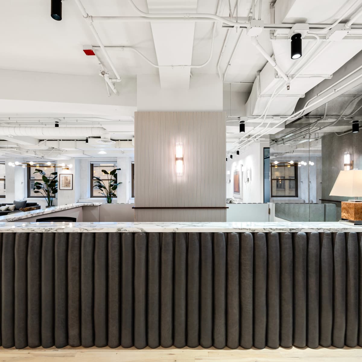 A modern reception desk with a curved, upholstered front, situated in a spacious, well-lit office lobby featuring contemporary furniture and decor.