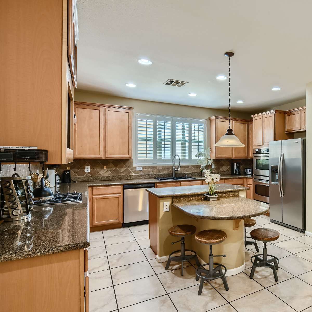 A modern kitchen with wooden cabinets, a central island with bar stools, and stainless steel appliances.