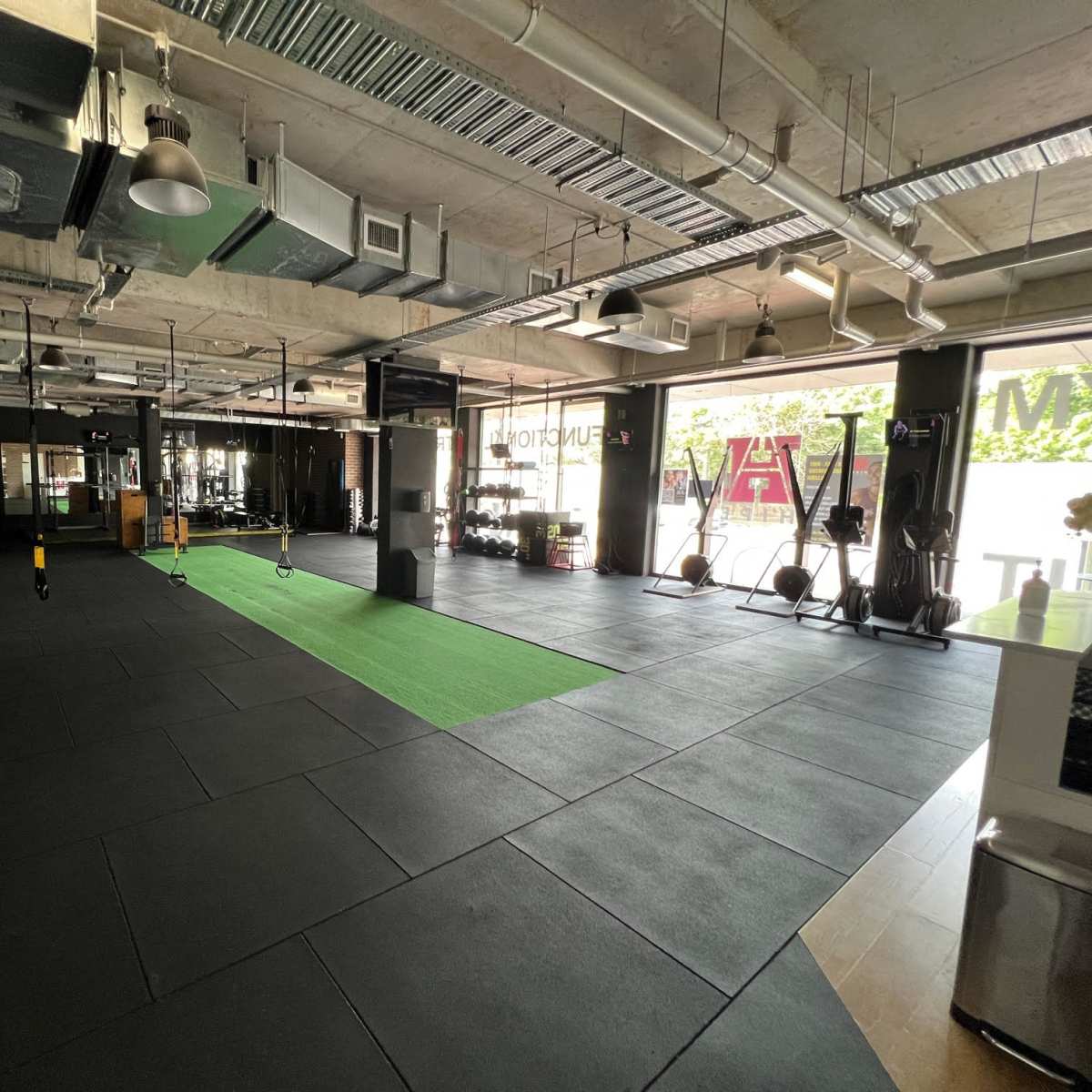 A spacious gym interior with black flooring, green turf in the center, and various exercise equipment along the walls.