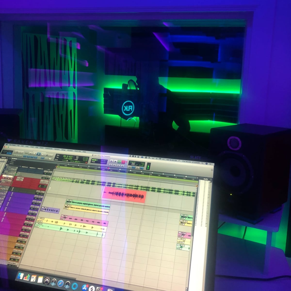 A music studio with a computer displaying audio editing software and colorful ambient lighting in the background.