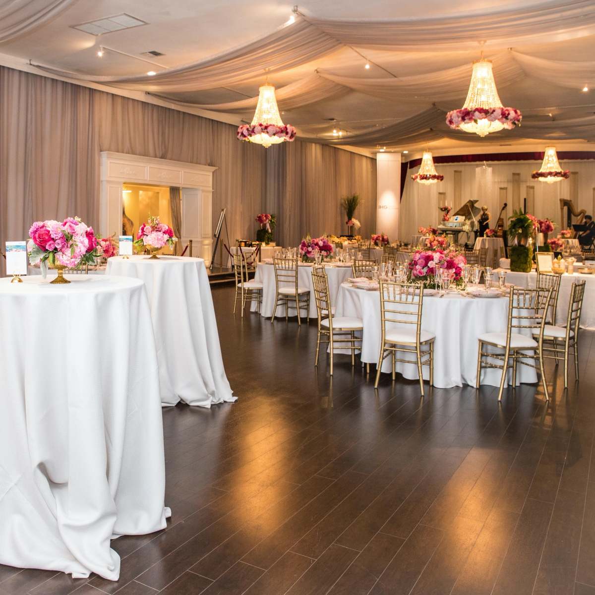 The venue features elegantly arranged tables with white linens, surrounded by floral decorations and soft lighting.