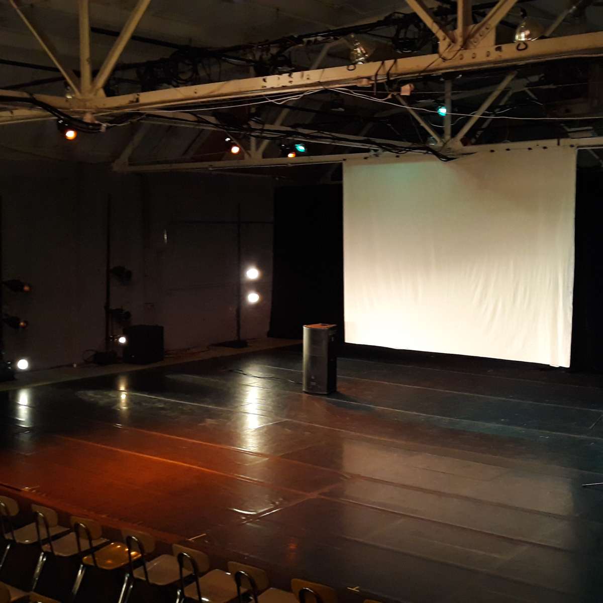 An empty stage in a theater with a large white projection screen and two microphones on stands facing the audience.