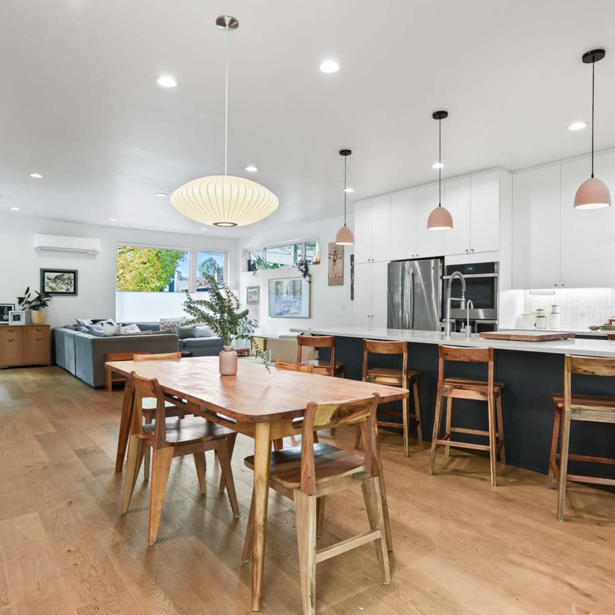 A modern kitchen and dining area features a wooden table surrounded by chairs, sleek cabinetry, and large windows allowing natural light to fill the space.