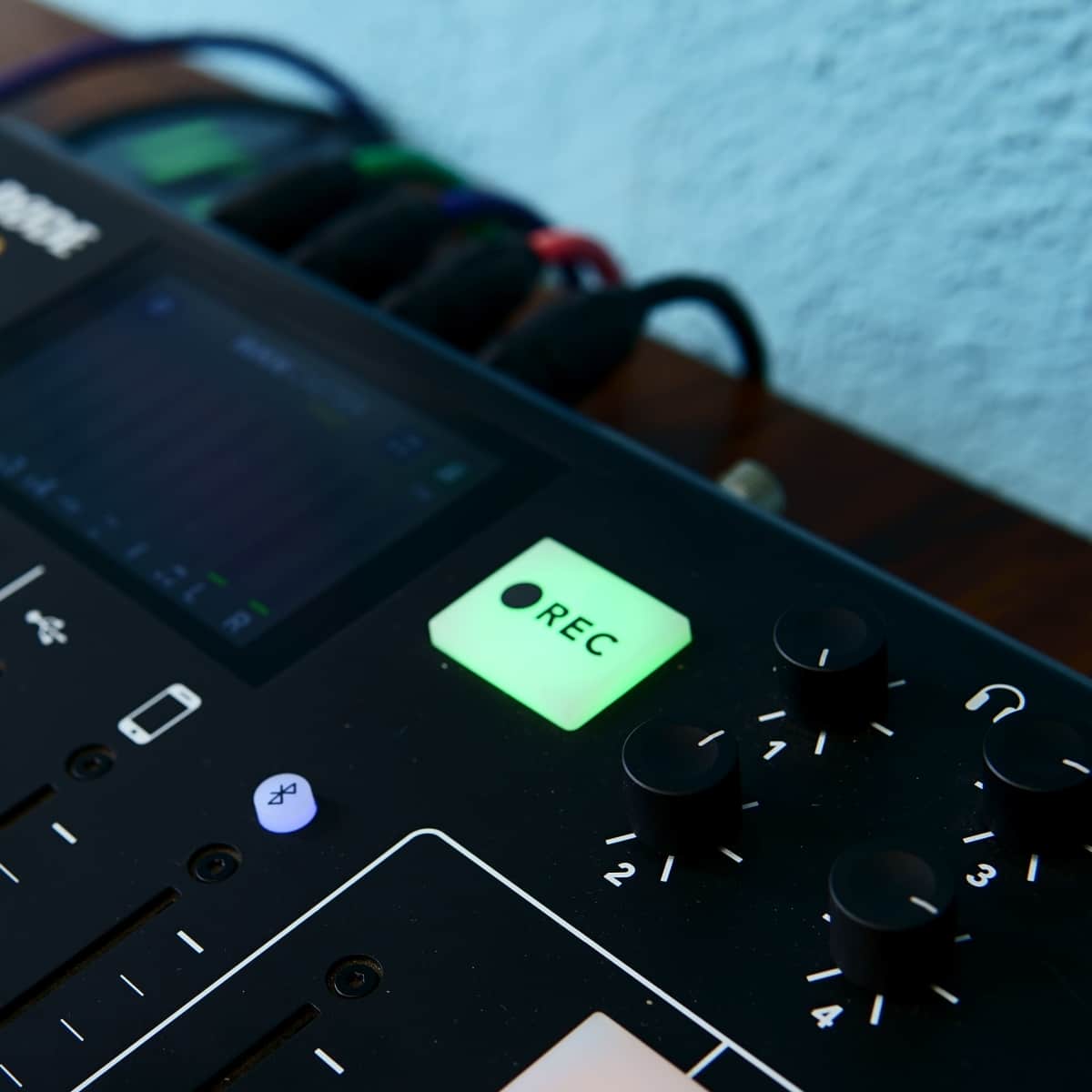 A close-up of a recording device with sliders, buttons, and a digital screen displaying audio levels.