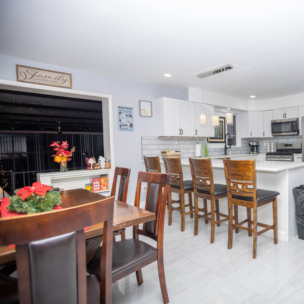 A modern kitchen with white cabinets, stainless steel appliances, a central island with seating, and a dining area featuring a wooden table.