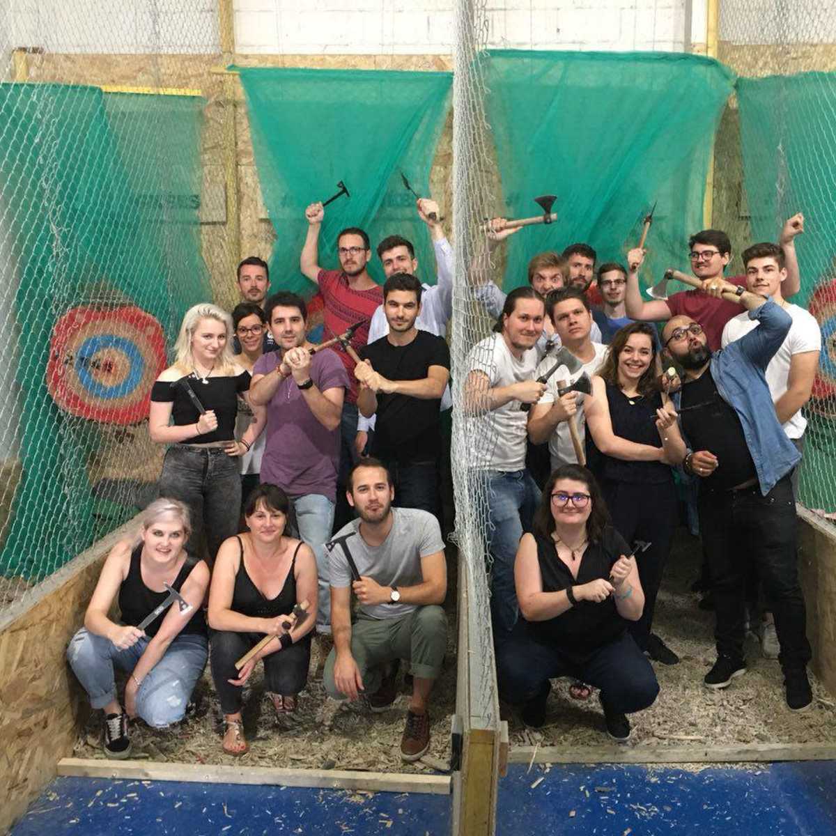 A large group of people poses with axes in an indoor axe-throwing venue, standing in front of target boards.