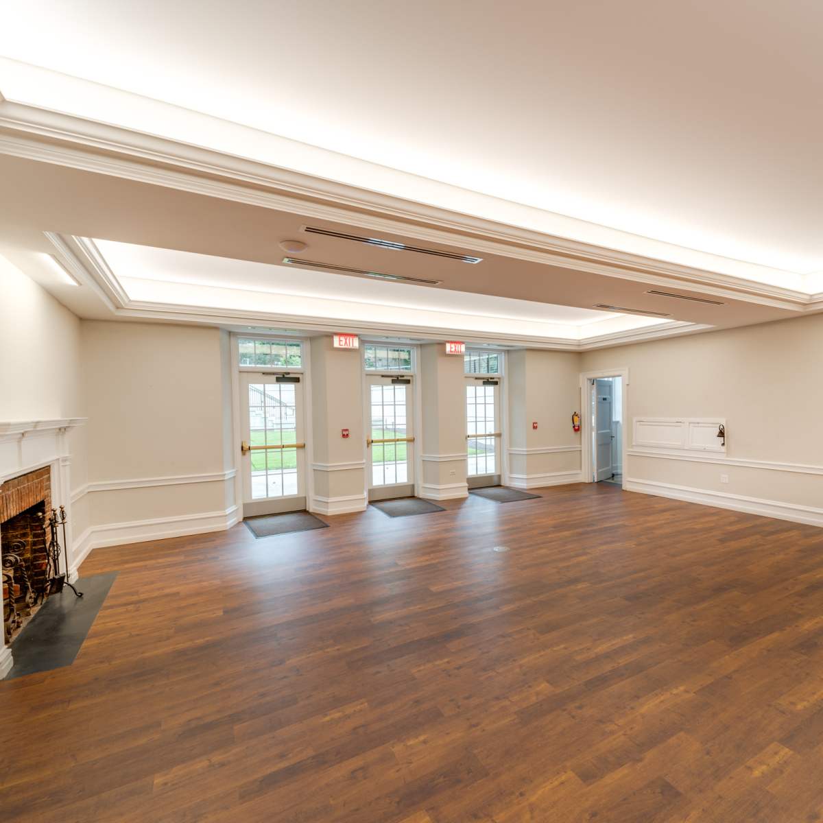 A spacious, empty room with hardwood flooring, large windows, and two sets of double doors leading outside.