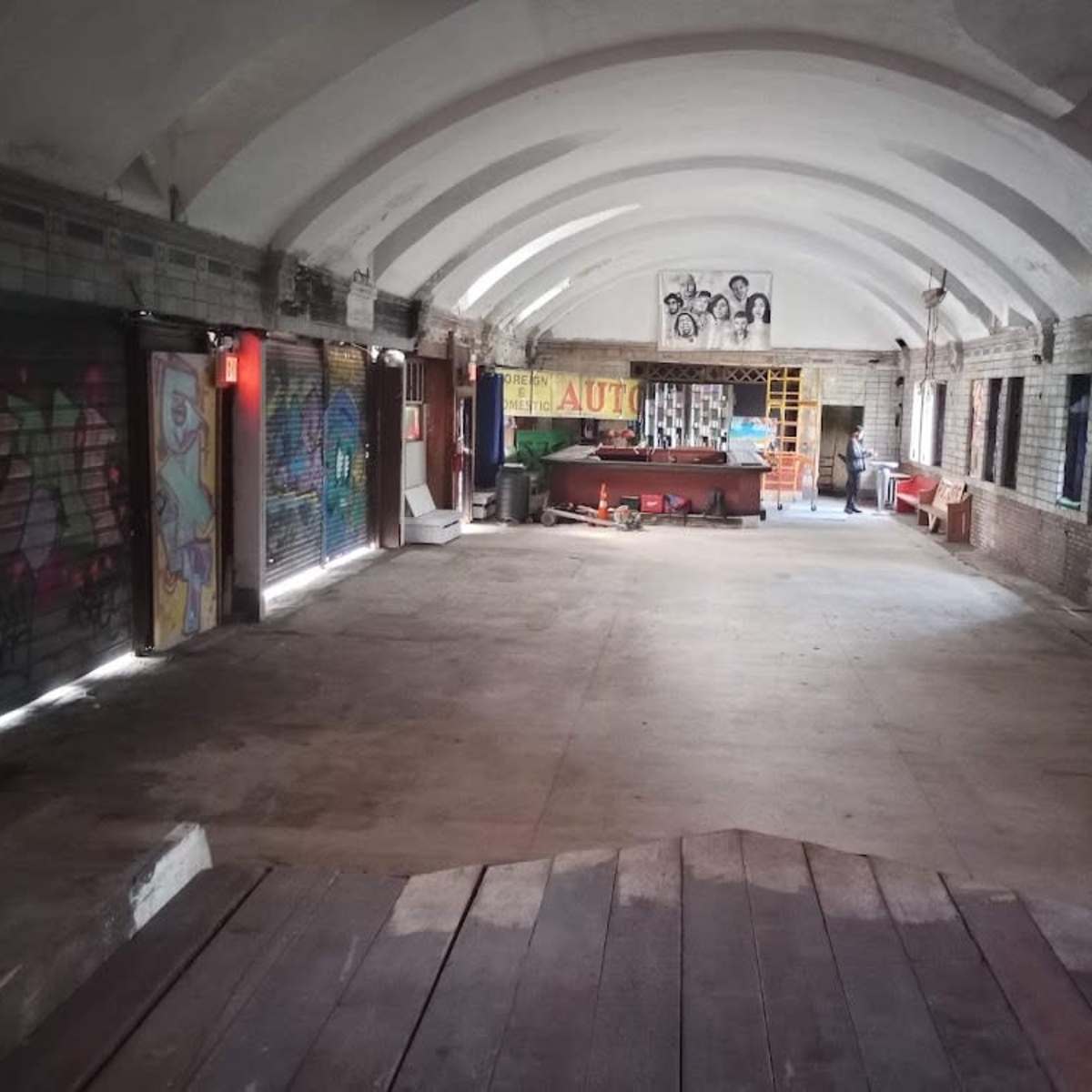 An empty, graffiti-covered room with an arched ceiling and exposed brick walls, featuring a central counter and various furniture scattered throughout.