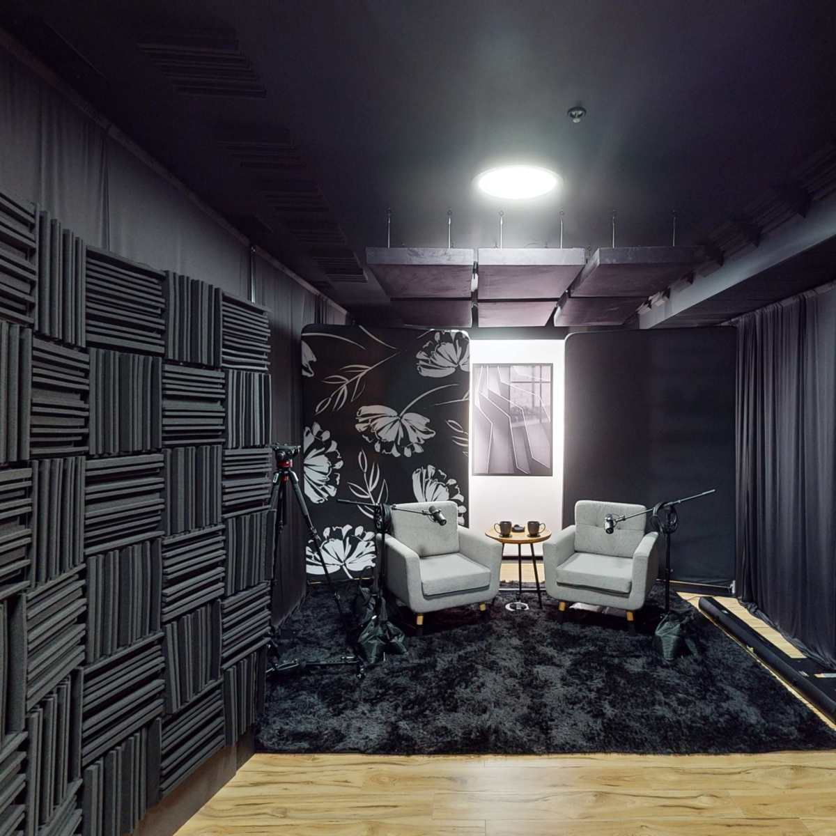 A recording studio featuring two armchairs, a small table, a black rug, and soundproofing panels on the walls.