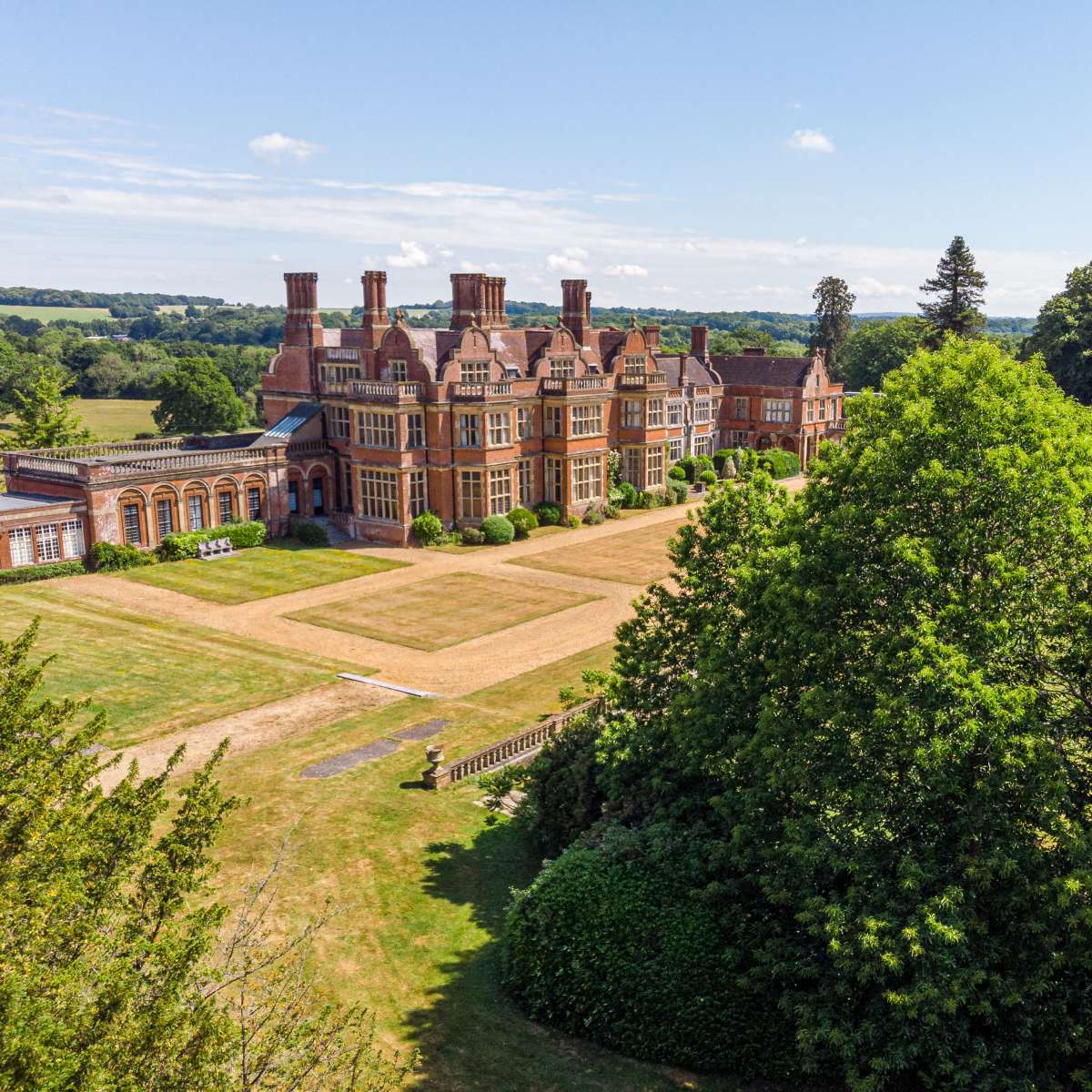 A large, ornate mansion surrounded by greenery and open fields under a clear blue sky.