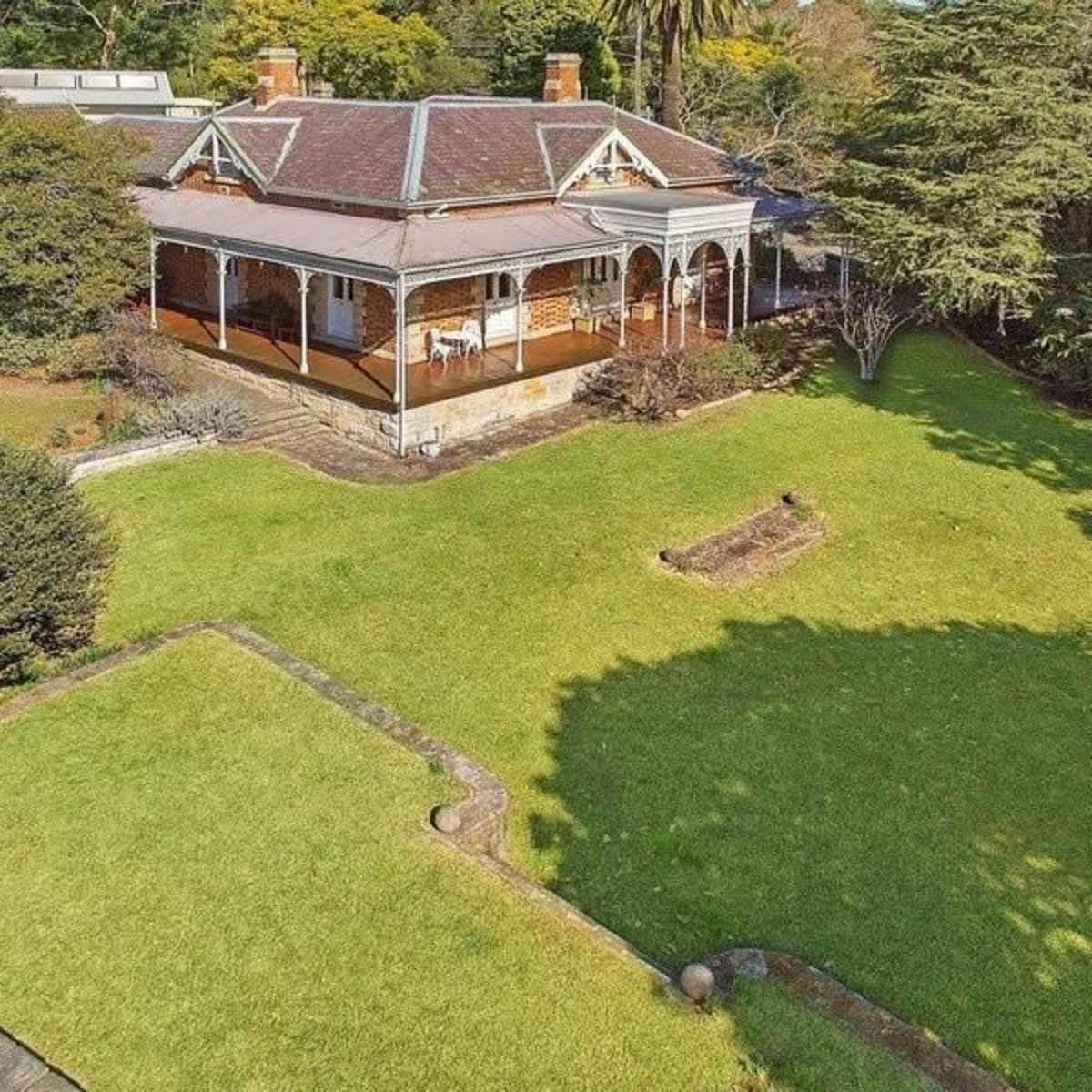 A large, single-story house with a veranda, surrounded by a spacious lawn and several trees.